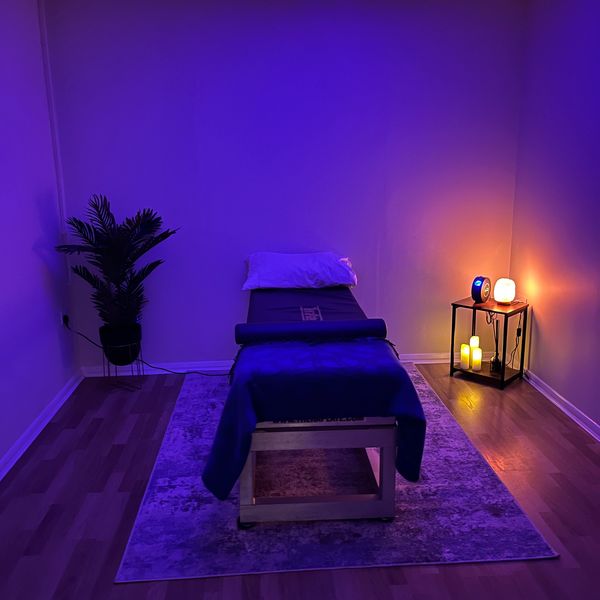 Massage table in a dimly lit room with calming purple and warm candlelight.