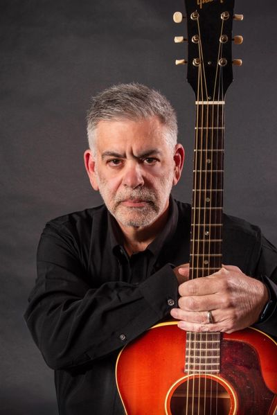 Man with gray hair holding an acoustic guitar.