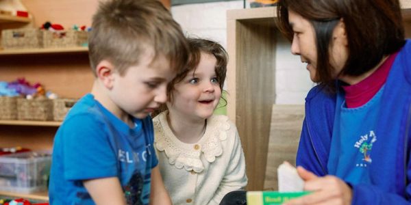 A teacher interacts warmly with two young children in a classroom setting.