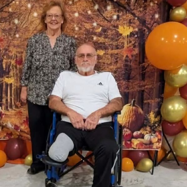A man in a wheelchair with a prosthetic leg and a woman standing behind him.