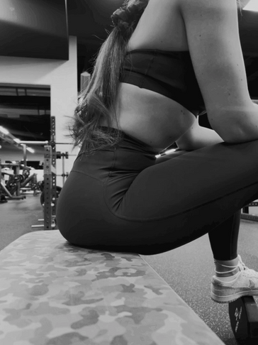 Woman in workout clothes sitting on a gym bench, resting between exercises.