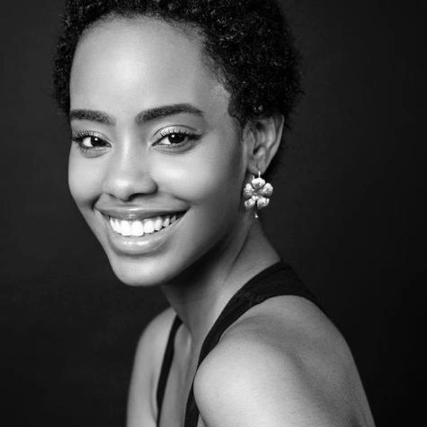 Cereyna Bougouneau smiles over her shoulder  in front of a black background in grayscale.
