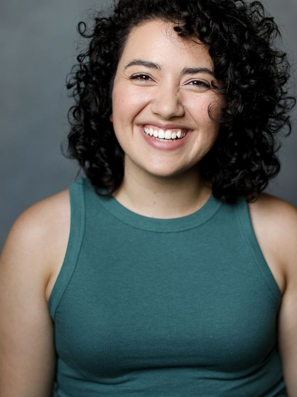 Laila Sahir smiles at the camera in front of a gray background.