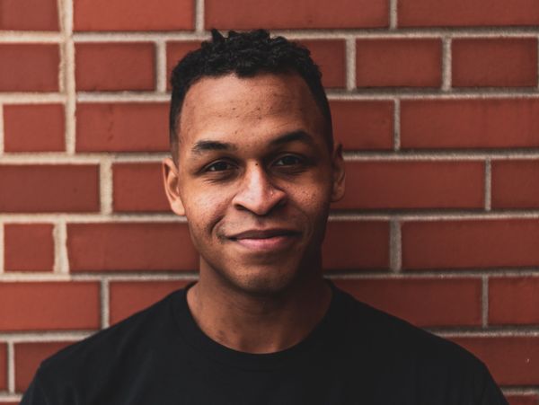 Dennis Lewis smiles at the camera in front of a brick background.