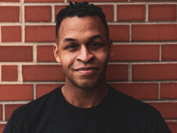 Dennis Lewis smiles at the camera in front of a brick background.