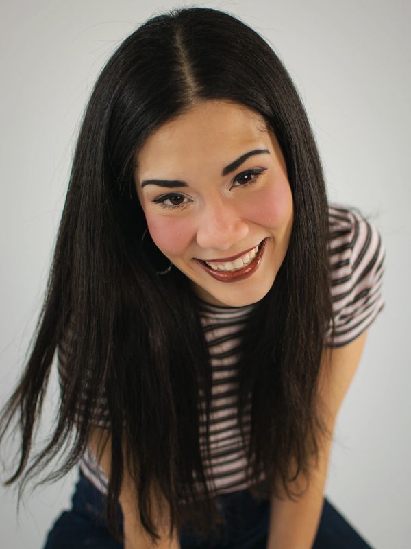 Ashley Oviedo leans toward and smiles at the camera in front of a white background.