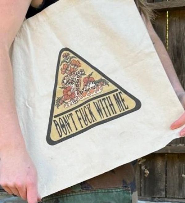 A beige tote bag with a snake and flowers, and the text 'DON'T FUCK WITH ME'.