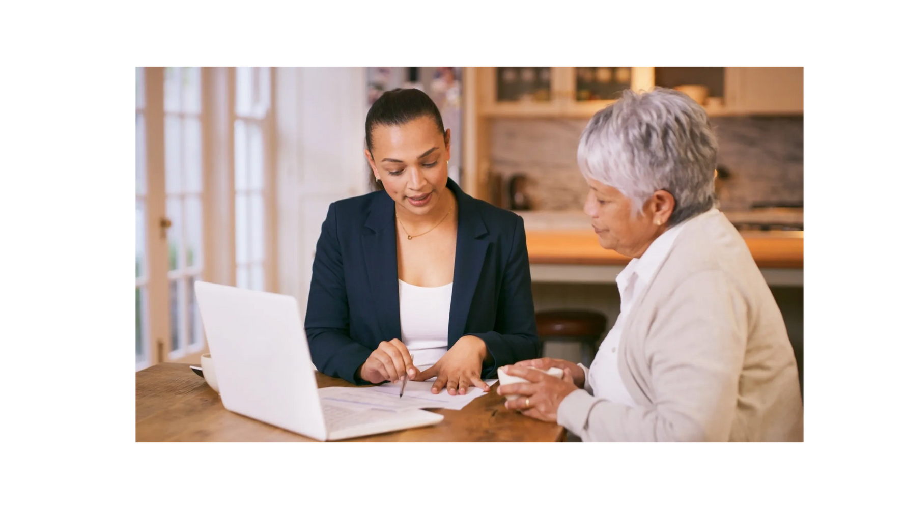 Two women discussing documents at a wooden table with a laptop.
