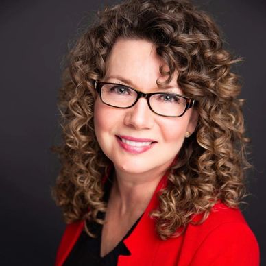 Professional woman with curly hair and glasses smiles warmly.