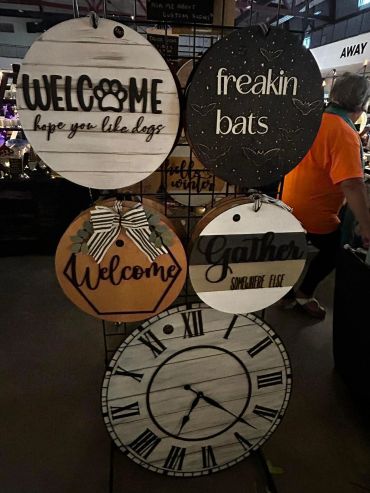 Decorative round signs with welcoming and Halloween themes displayed at a market booth.