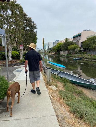 Mitchel walking with Luke along the Venice canal with boats and canoe and trees  