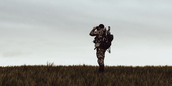 Archery hunter glassing on a grassy hill.