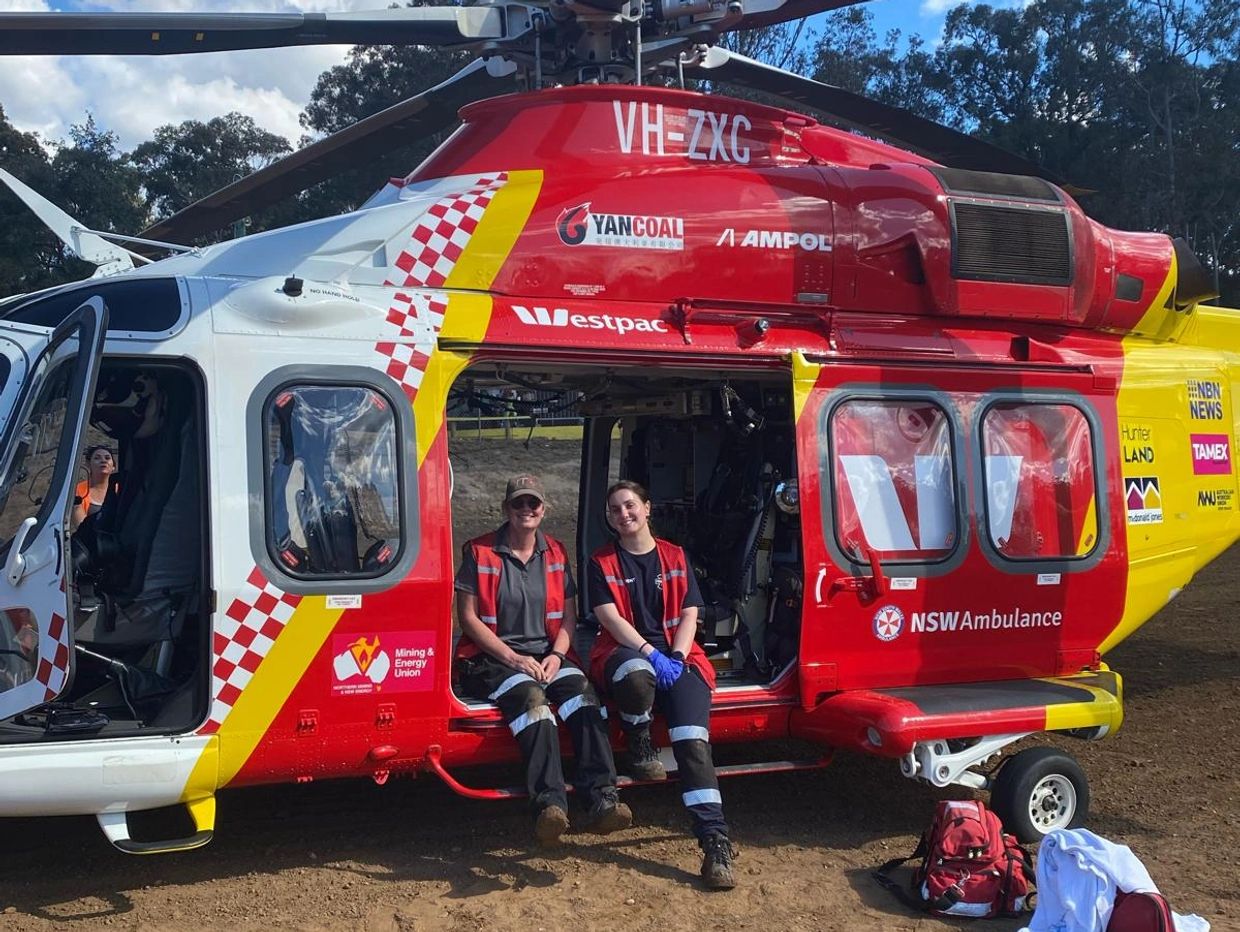 Two medical workers sitting on the step of a red and yellow NSW Ambulance helicopter.