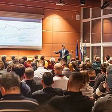 A speaker presents data to a large audience in a conference room.