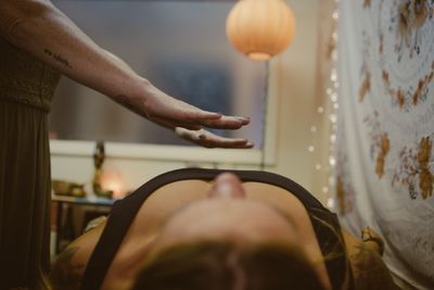 A person practicing energy healing over a lying individual in a calm room.
