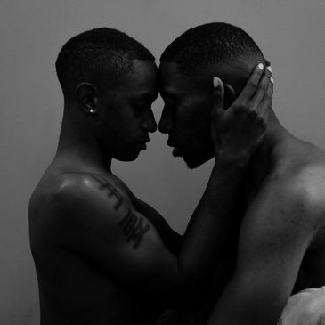 Two shirtless men in an intimate, tender moment, foreheads touching.