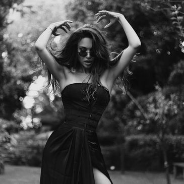 Woman in a black dress striking a pose in a garden.