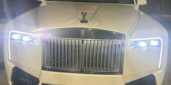 Front view of a white Rolls-Royce with headlights on at night.