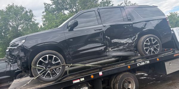 Damaged black Chevrolet Suburban on a tow truck with side impact.