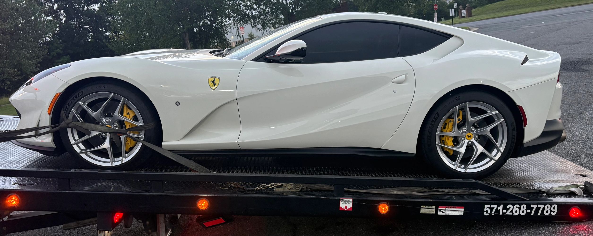 White Ferrari sports car secured on a flatbed tow truck.