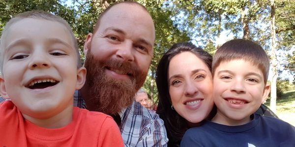 A happy family of four smiling outdoors on a sunny day.