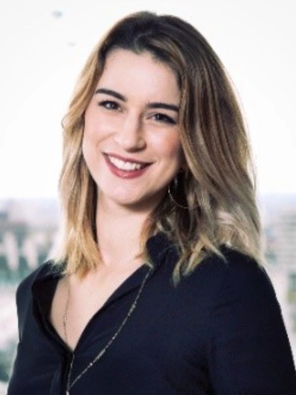 Young woman with blonde hair smiling against a blurred urban background.