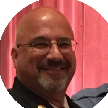 Smiling man with glasses and goatee in front of red curtain.