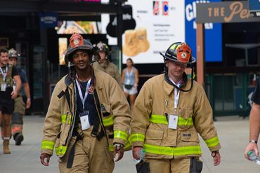 Two firefighters in uniform walking on a city street.