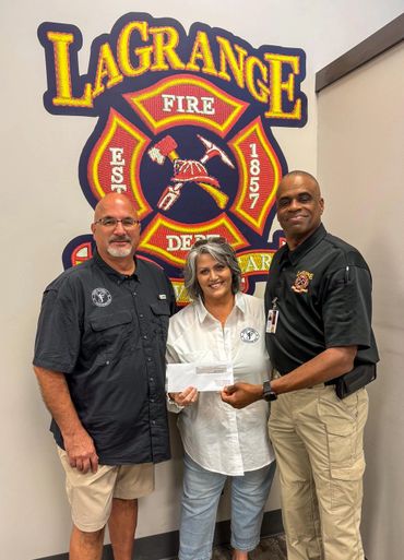 Three people stand in front of a LaGrange Fire Department emblem, holding a check.