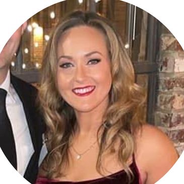 Smiling woman with wavy hair in a maroon dress at an indoor event.