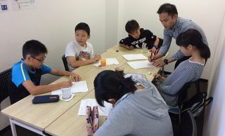 A teacher helps children with their schoolwork around a table.
