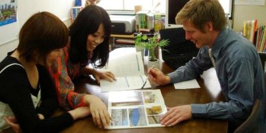 Three people reviewing a book together at a table.