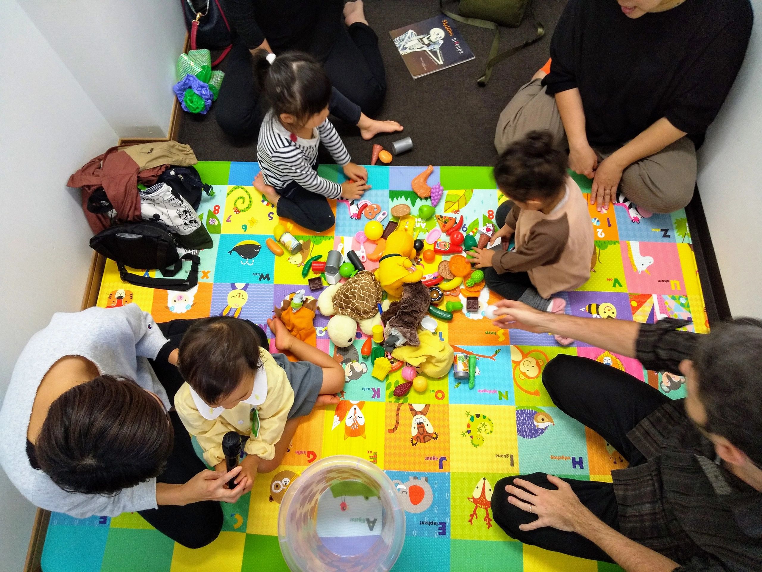 親子英会話クラスで赤ちゃんと幼児がカラフルなアルファベットマットの上でネイティブ講師と英語を遊びながら学ぶ様子