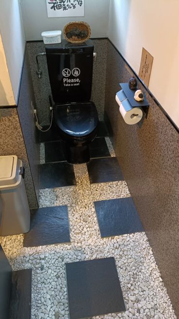 Compact bathroom with a black toilet and pebble stone floor.
