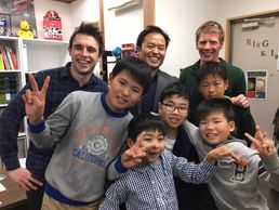 A cheerful group of adults and children posing with peace signs indoors.