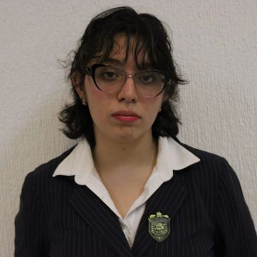 Young woman in glasses and formal attire posing against a plain background.