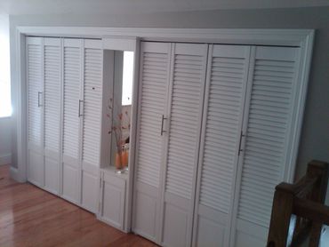 White louvered closet doors with a built-in mirror and vase on a wooden floor.