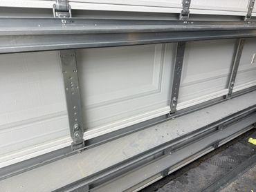 Partially opened white garage door with metal frames and hinges.