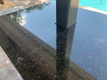 Glossy black granite countertop with a metal post near a pool.