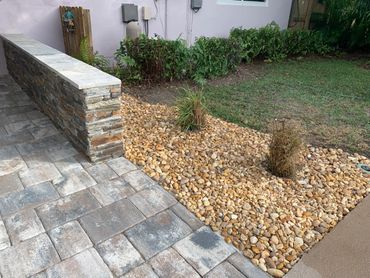 Stone wall, paved patio, and decorative rock garden with plants.
