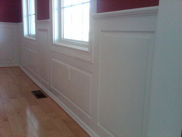 White wainscoting panels on a wall with windows and hardwood floor.