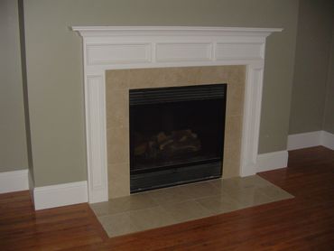 A modern fireplace with beige tiles and white mantel in a room with wooden floors.