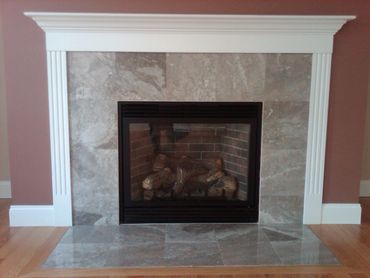 Modern fireplace with marble tiles and white mantle on wooden floor.