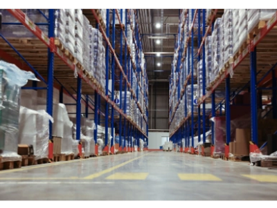 Wide aisle in a large warehouse with tall shelves stocked with goods.