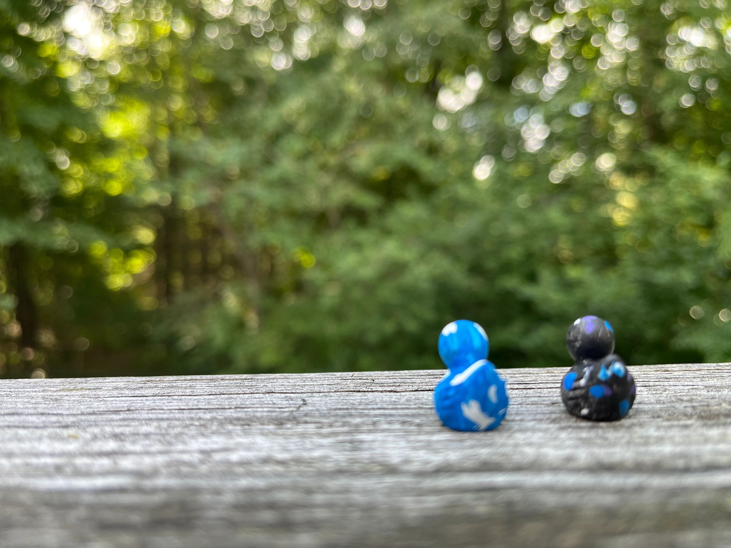 Two painted figurines on a wooden surface with a blurred green background.