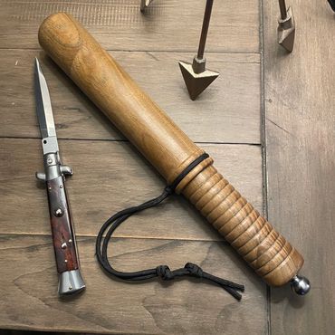 Wooden baton and switchblade knife on a wooden surface.