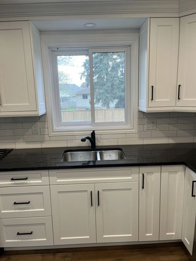 Modern kitchen with white cabinets, black countertop, and a window above the sink.
