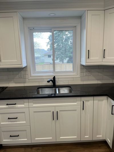 Modern kitchen with white cabinets, black countertop, and a window above the sink.