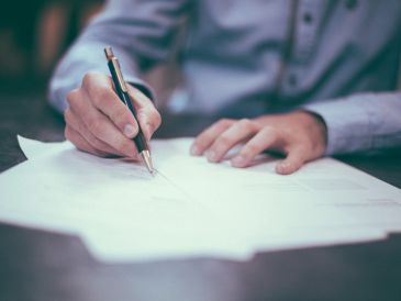 Person signing a document with a pen on a table.