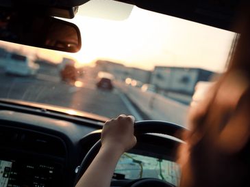 Person driving a car during sunset on a highway.